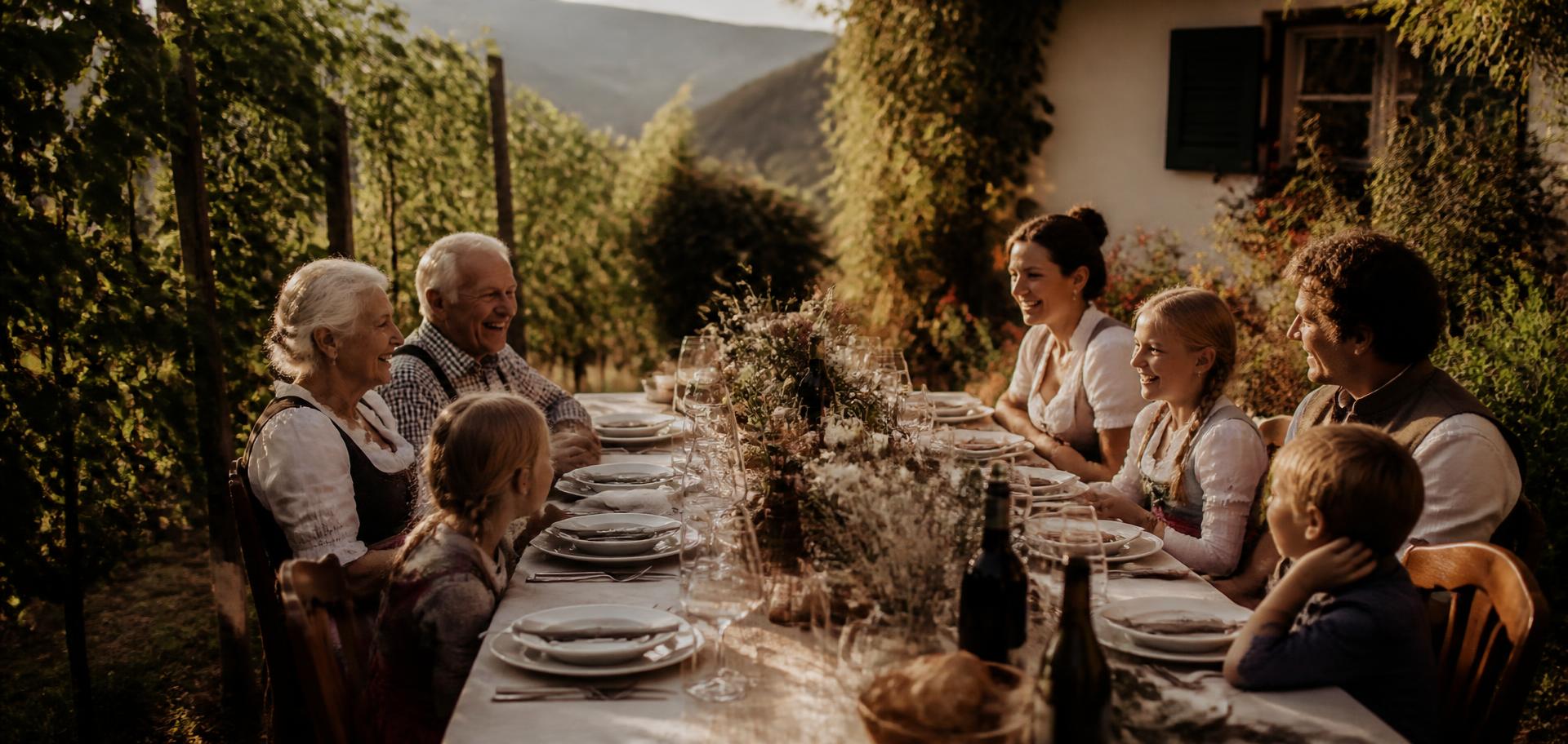 Familie an einer langen gedeckten Tafel im Garten des Pinzonerkellers zwischen den Reben